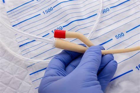 Gloved hand holding a Foley catheter and tubing near a urinary drainage bag for medical care