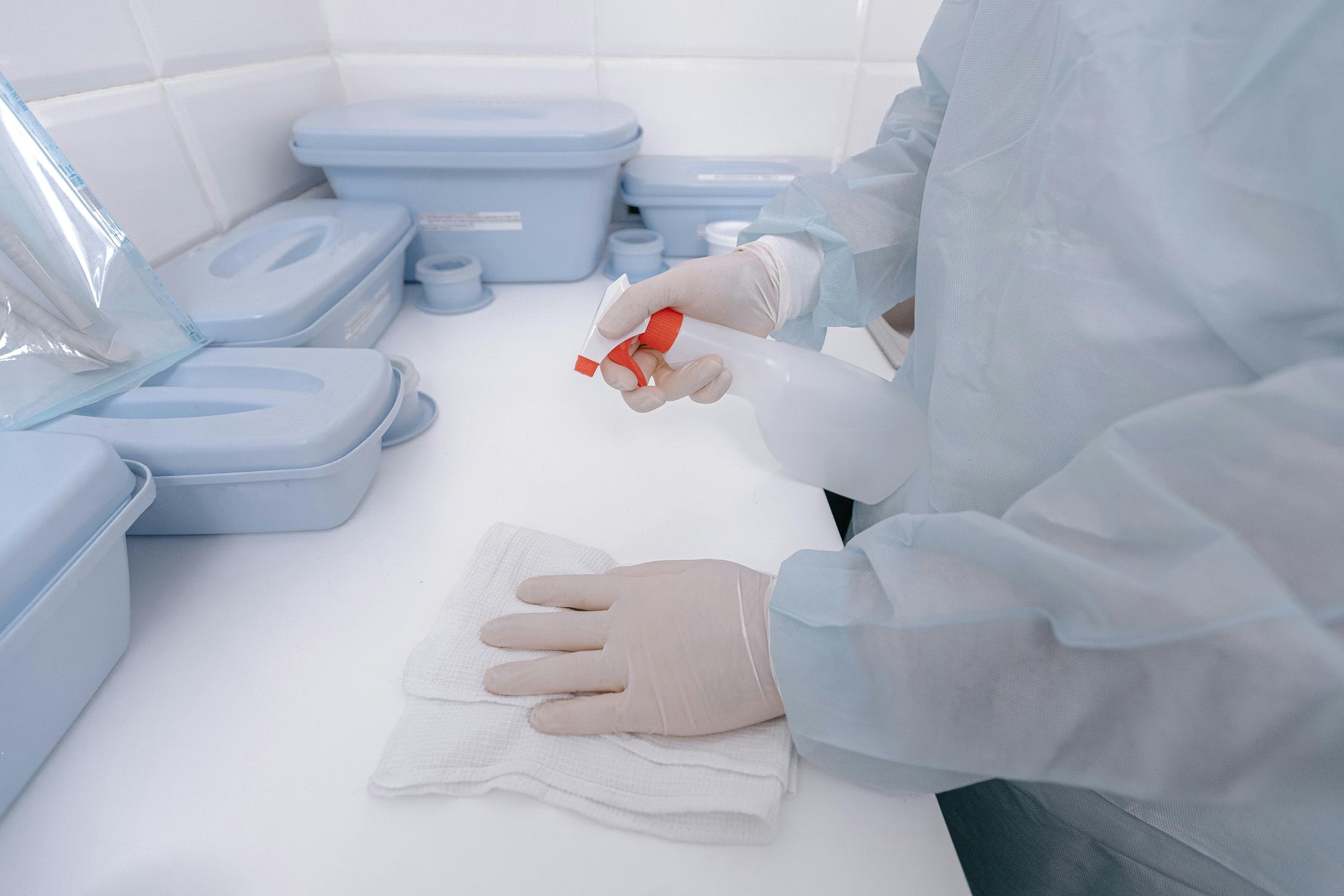 Medical professional sanitizing surface with spray and cloth, surrounded by PPE and medical supplies