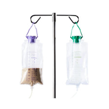 Two medical feeding bags hanging on an IV pole, one with brown liquid, used for enteral feeding.